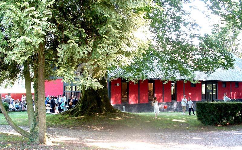 Un bâtiment rouge entouré d'arbres dans un parc, avec des personnes rassemblées à l'extérieur.