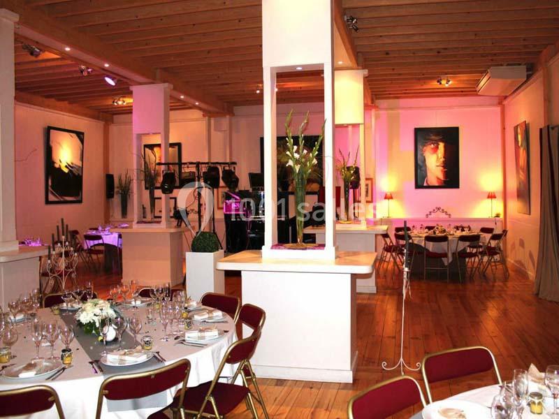 Salle de réception décorée avec des tables dressées, des chaises rouges et des œuvres d'art accrochées aux murs.