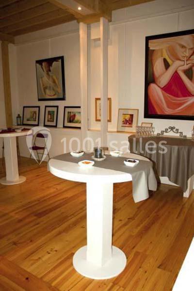 Salle d'exposition avec des œuvres d'art accrochées aux murs et des tables blanches disposées sur un sol en bois.