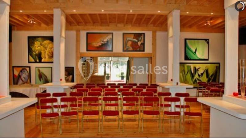 Salle lumineuse avec des rangées de chaises rouges, des colonnes blanches et des tableaux colorés accrochés aux murs.