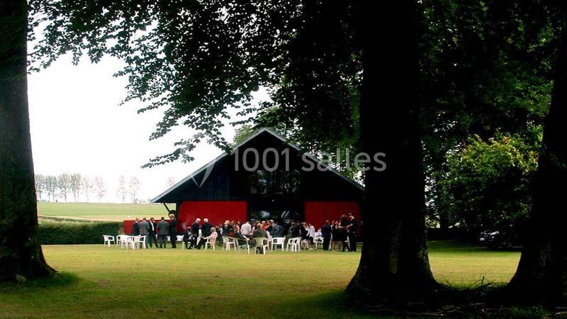 Groupe de personnes rassemblées devant un bâtiment rouge et noir dans un grand espace vert entouré d'arbres.