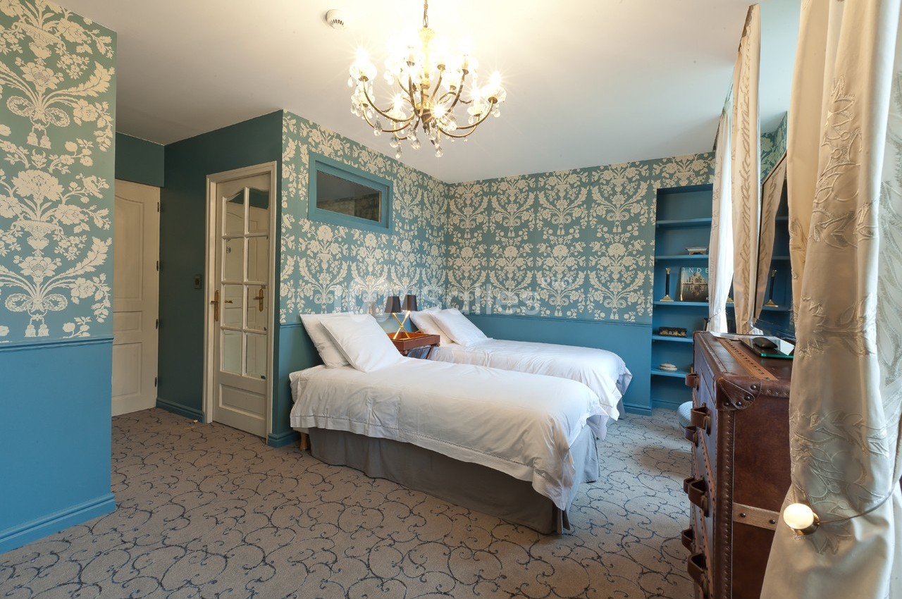 Chambre lumineuse avec deux lits simples, murs bleu à motifs, lustre et mobilier en bois.