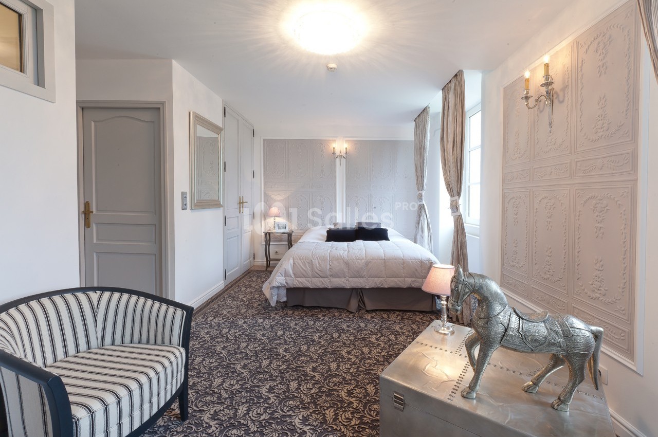 Chambre lumineuse avec lit double, fauteuil rayé, tapis à motifs et décoration élégante incluant un cheval argenté.