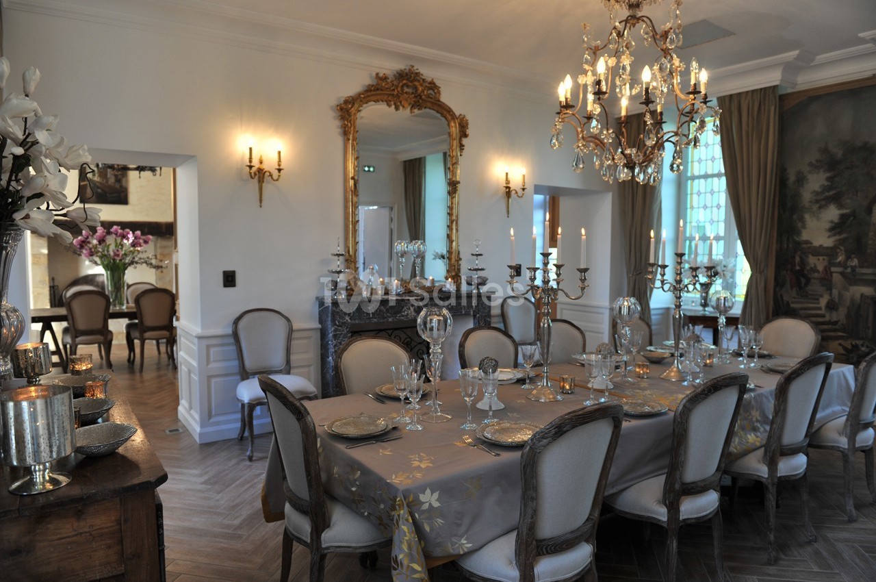 Salle à manger élégante avec table dressée, chandelier, miroir doré et éclairage chaleureux.