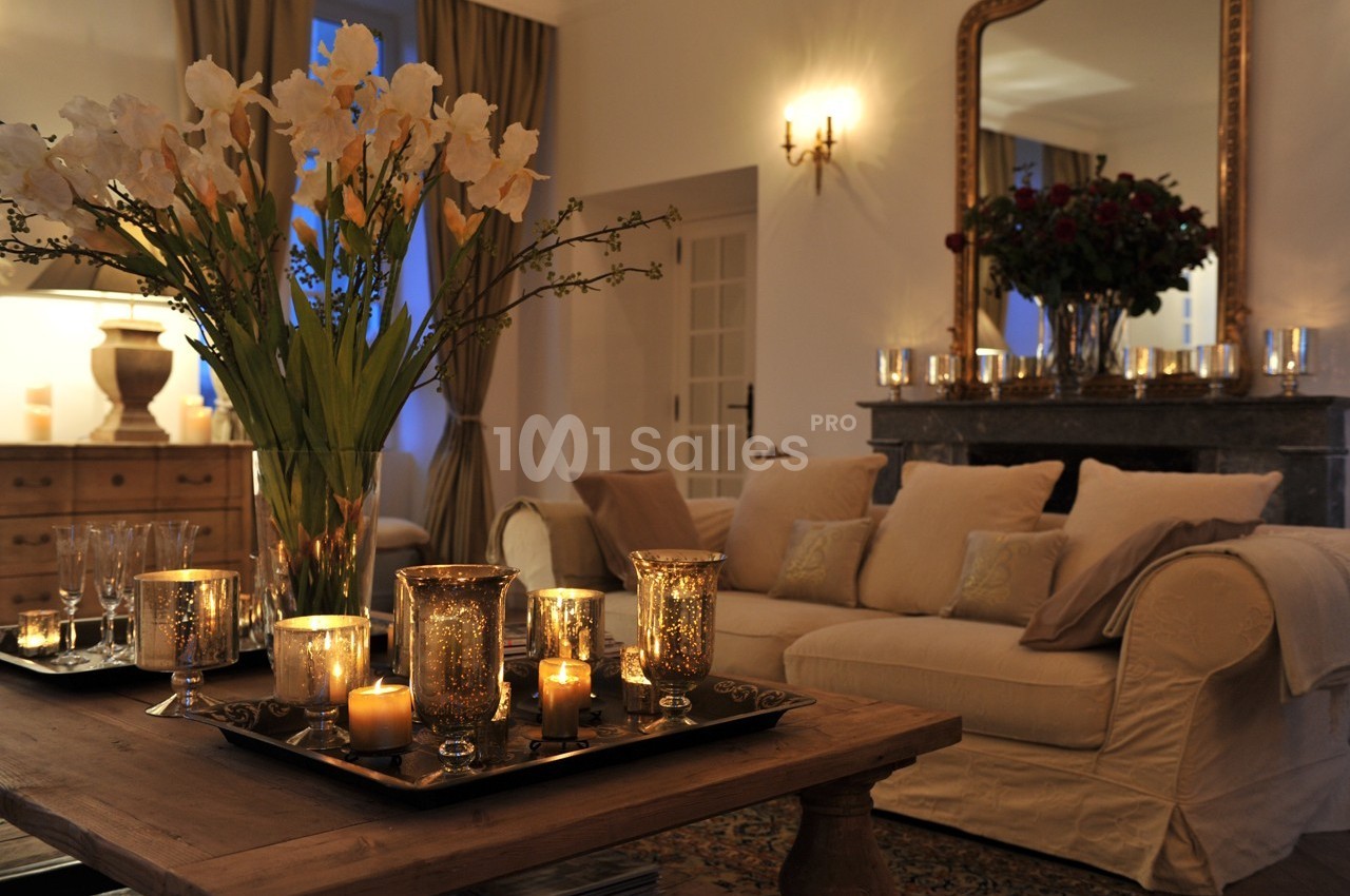 Salon chaleureux avec canapé beige, table en bois ornée de bougies et vase de fleurs, éclairage tamisé.