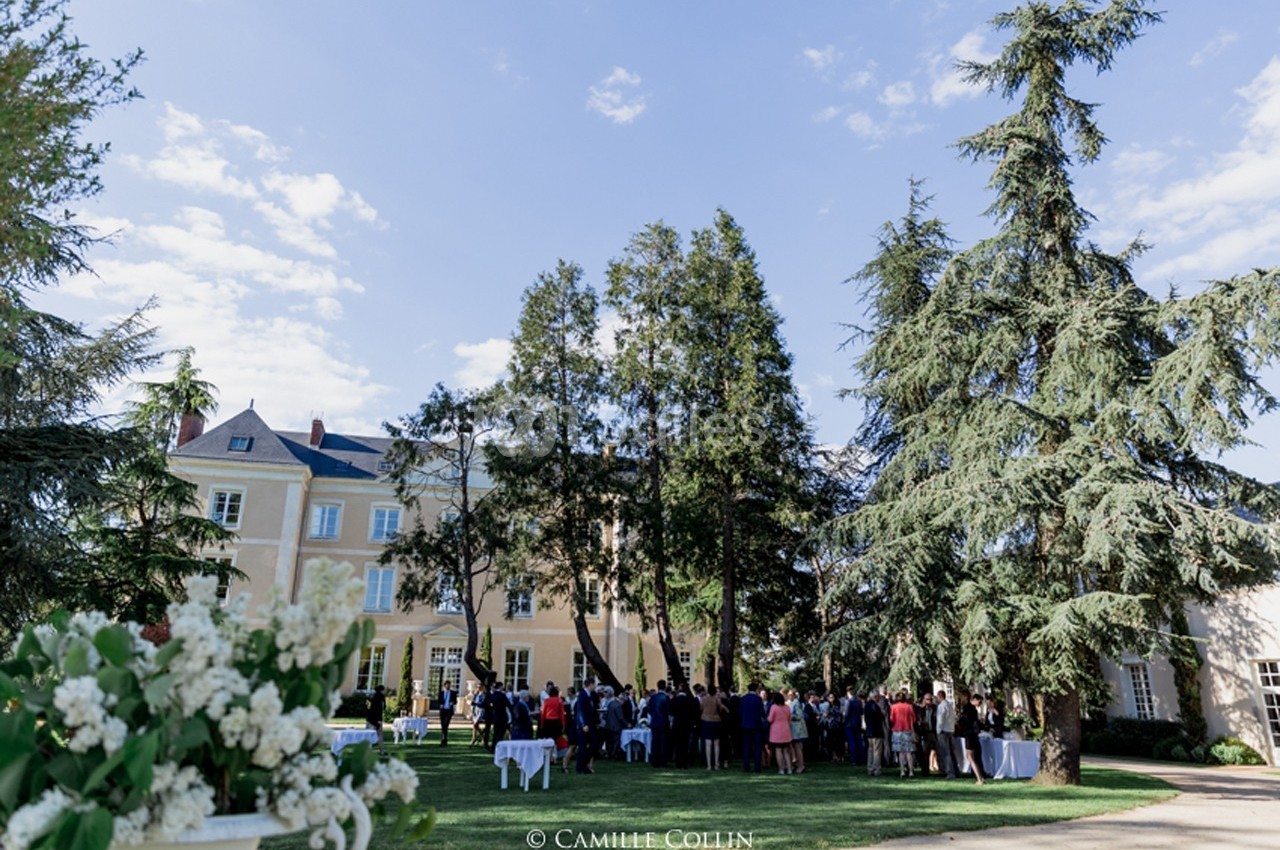 Groupe de personnes rassemblées dans le jardin d'un grand bâtiment entouré d'arbres par une journée ensoleillée.
