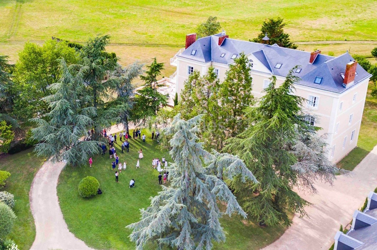 Vue aérienne d'un grand bâtiment entouré d'arbres, avec un groupe de personnes rassemblées sur la pelouse.