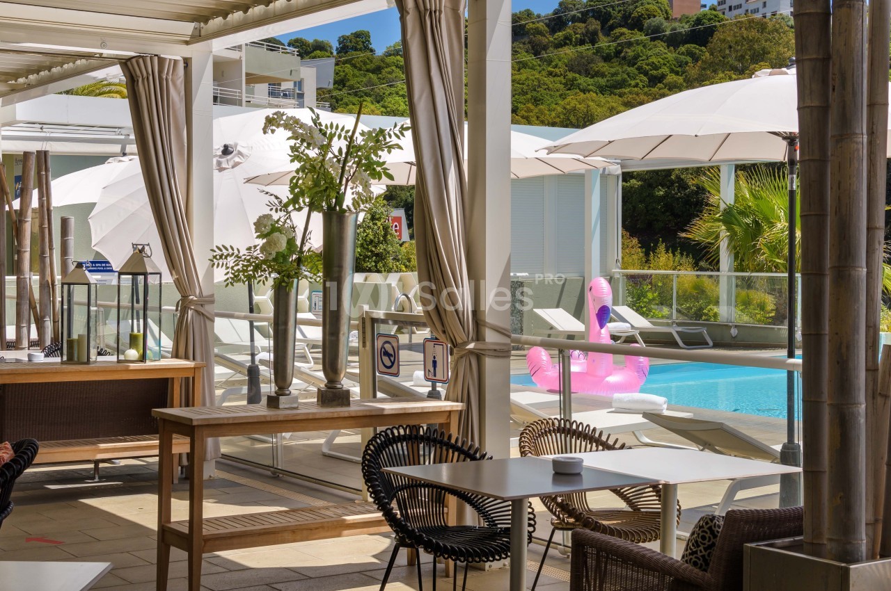 Espace extérieur avec tables, chaises, parasols et vue sur une piscine équipée de bouées gonflables.