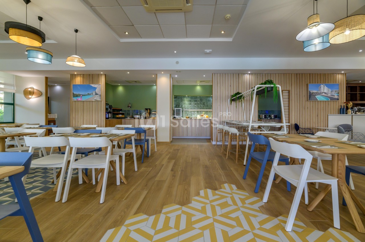 Salle de restaurant lumineuse avec tables et chaises modernes, décoration en bois et éclairage suspendu.