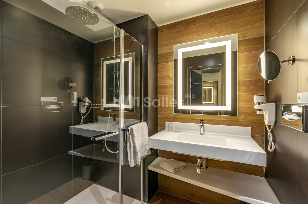 Salle de bain moderne avec douche à l'italienne, lavabo blanc, miroir éclairé et murs en bois et carrelage sombre.