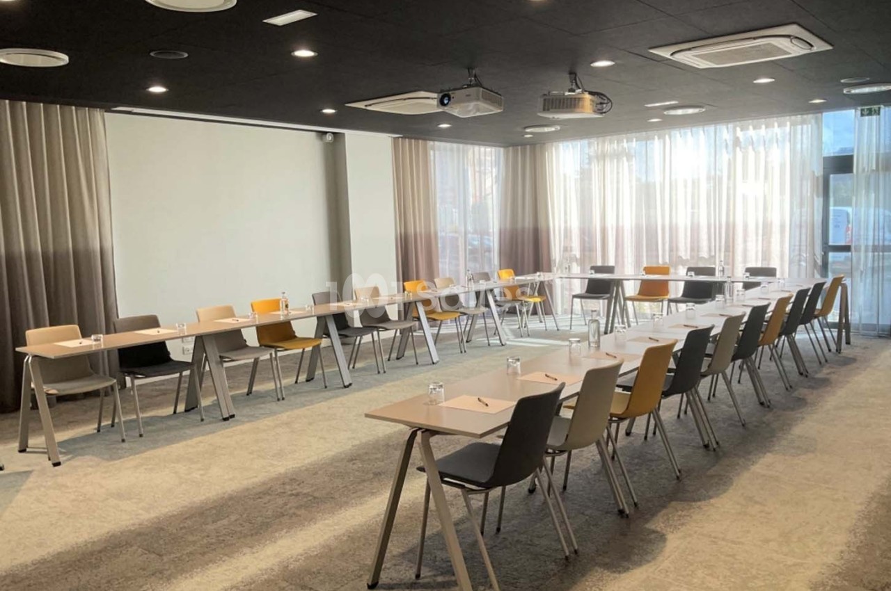 Salle de réunion lumineuse avec des tables et des chaises disposées en U, équipée de projecteurs au plafond.