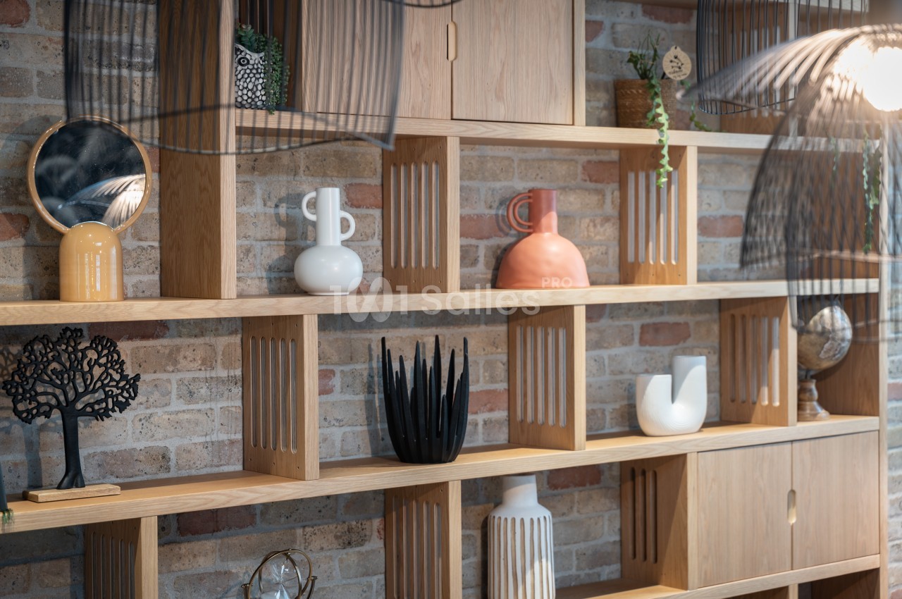 Étagère en bois clair contre un mur de briques, décorée d'objets variés comme vases, plantes et sculptures.