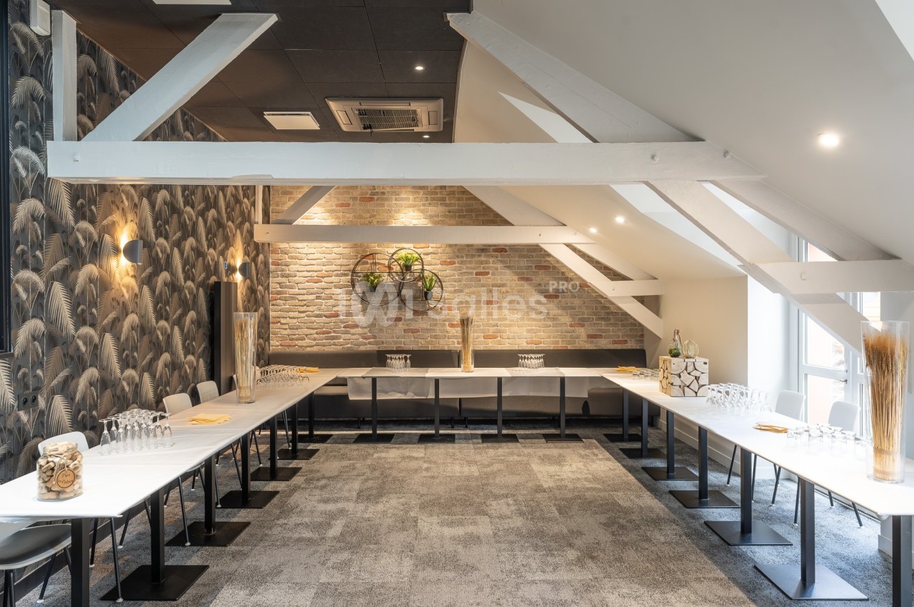Salle de réunion lumineuse avec tables disposées en U, murs en briques et décorations modernes.
