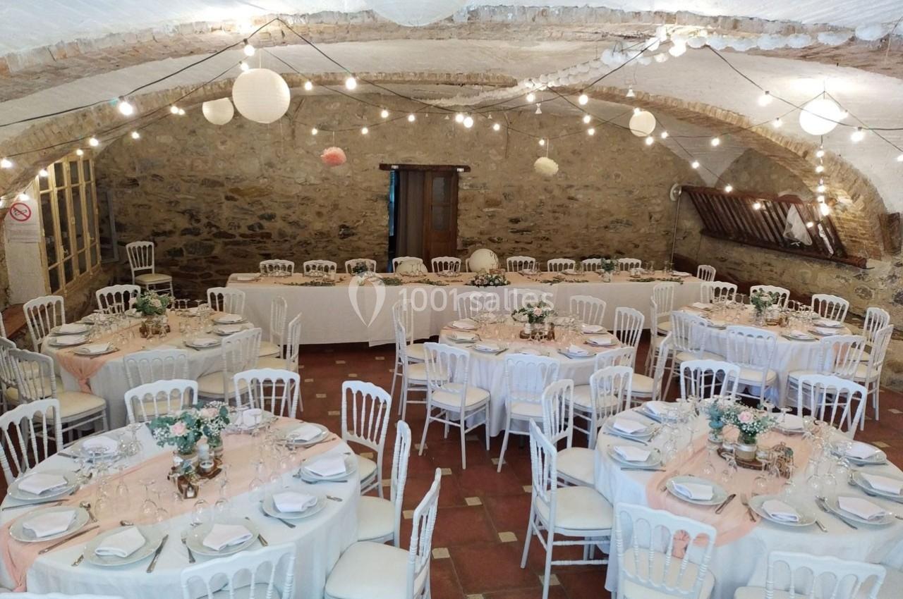 Salle de réception décorée avec des tables rondes, nappes blanches, chaises assorties et guirlandes lumineuses suspendues.