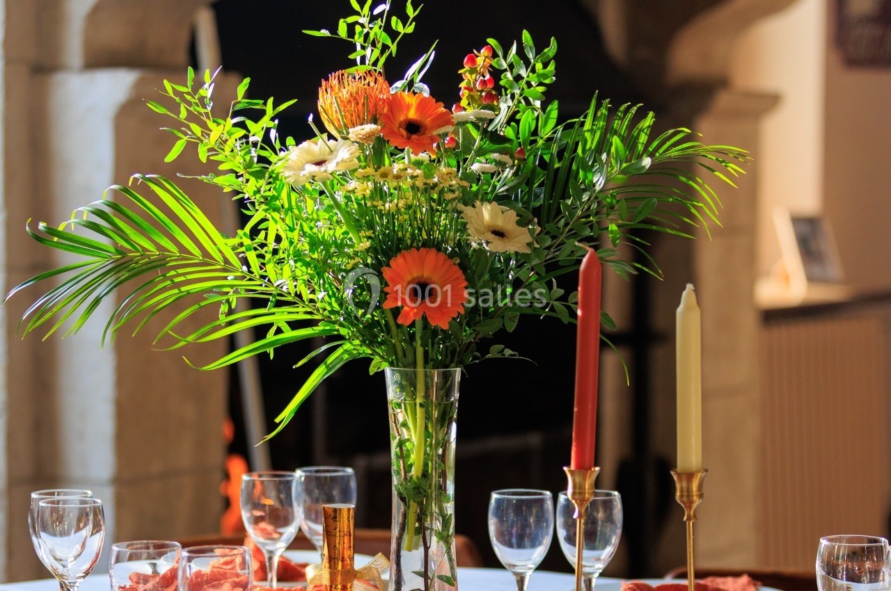Bouquet de fleurs colorées dans un vase en verre, posé sur une table dressée avec des verres et des bougeoirs.