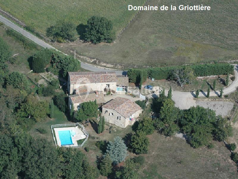 Vue aérienne d'un domaine rural avec bâtiments en pierre, piscine, arbres et chemins entourés de champs.