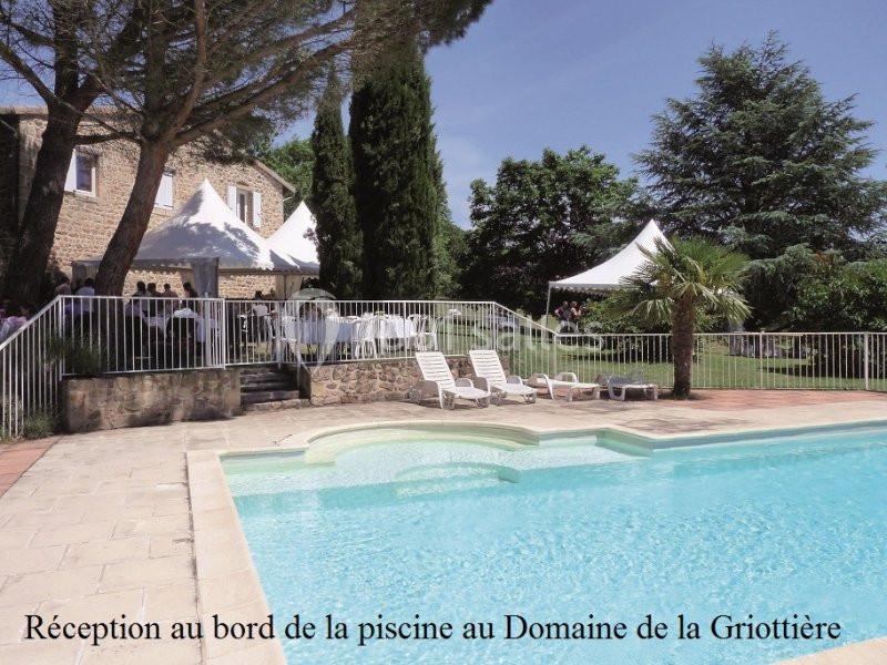 Piscine extérieure entourée de chaises longues, avec une réception sous des tentes blanches près d'un bâtiment en pierre.