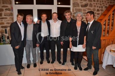 Un groupe de personnes posant debout dans une pièce avec des murs en pierre et une table en arrière-plan.