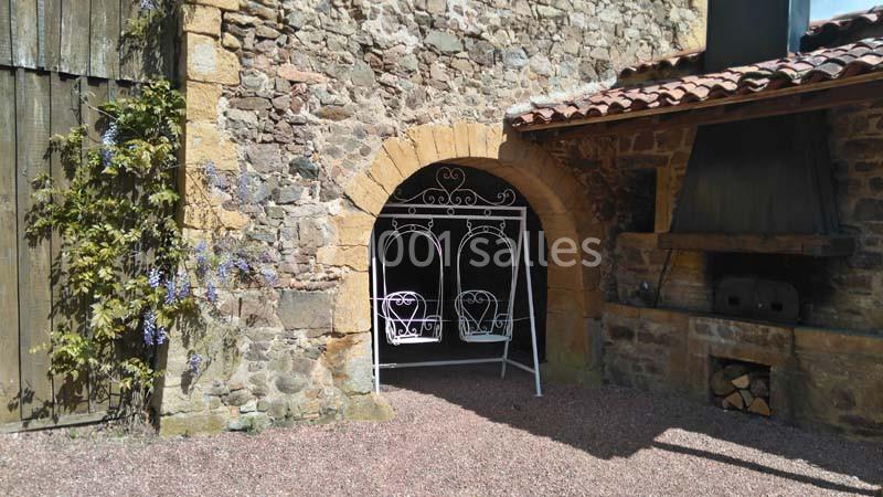 Banc en fer forgé blanc sous une arche en pierre, adossé à un mur de pierre avec des glycines grimpantes.