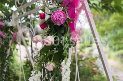 Décoration florale composée de roses, pivoines et feuillage, accrochée à une structure blanche en extérieur.