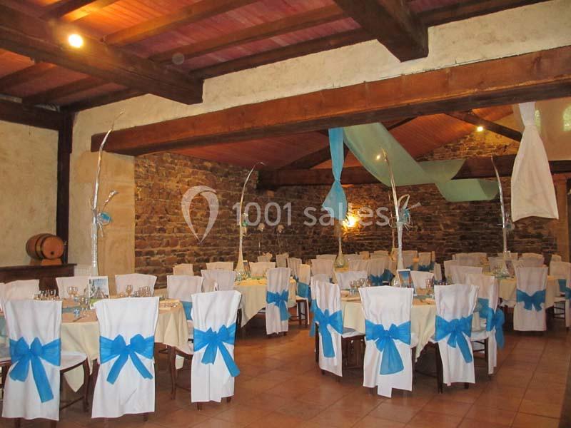 Salle de réception décorée avec des chaises blanches ornées de nœuds bleus et des tables dressées sous un plafond en bois.