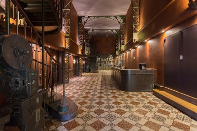 Hall spacieux avec sol en mosaïque, arches illuminées et tables décorées, éclairage chaleureux et ambiance élégante.