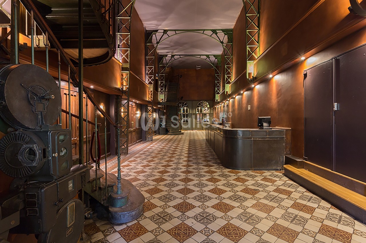 Intérieur d'un hall spacieux avec un sol carrelé, un escalier en colimaçon et un comptoir d'accueil en métal.