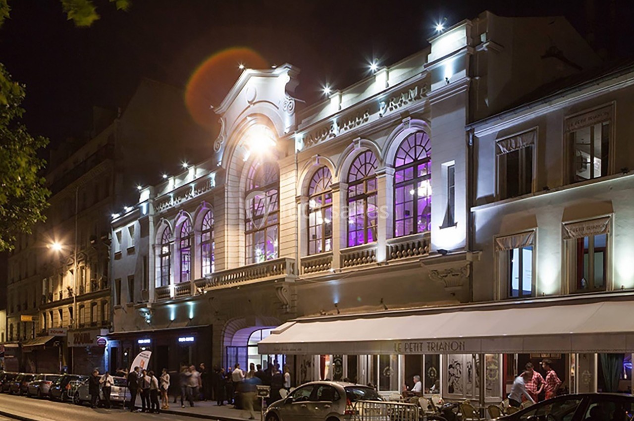 Façade illuminée d'un bâtiment ancien avec des arches et des fenêtres, vue de nuit sur une rue animée.