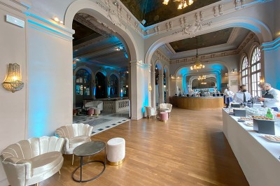 Hall spacieux avec sol en mosaïque, arches illuminées et tables décorées, éclairage chaleureux et ambiance élégante.