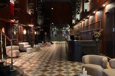 Hall spacieux avec sol en mosaïque, arches illuminées et tables décorées, éclairage chaleureux et ambiance élégante.