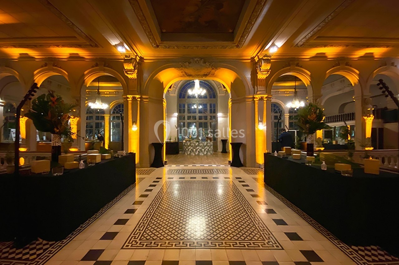 Hall spacieux avec sol en mosaïque, arches illuminées et tables décorées, éclairage chaleureux et ambiance élégante.
