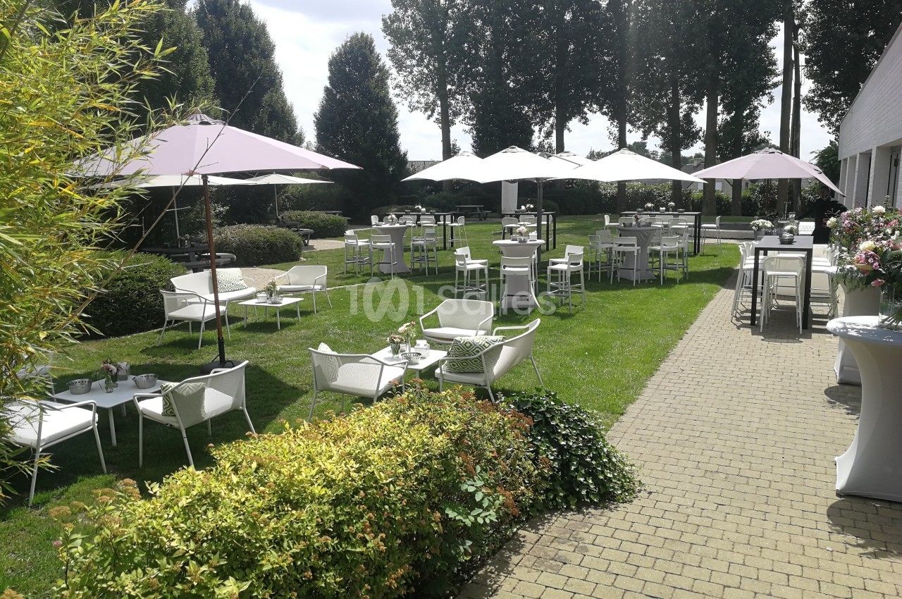 Terrasse extérieure avec tables, chaises blanches et parasols, entourée de verdure et d'arbres.