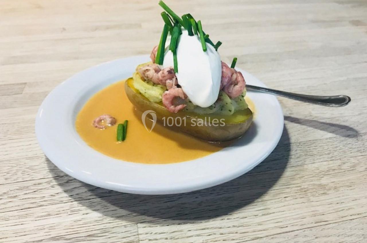 Pomme de terre garnie de crevettes, crème fraîche et ciboulette, servie avec une sauce sur une assiette blanche.