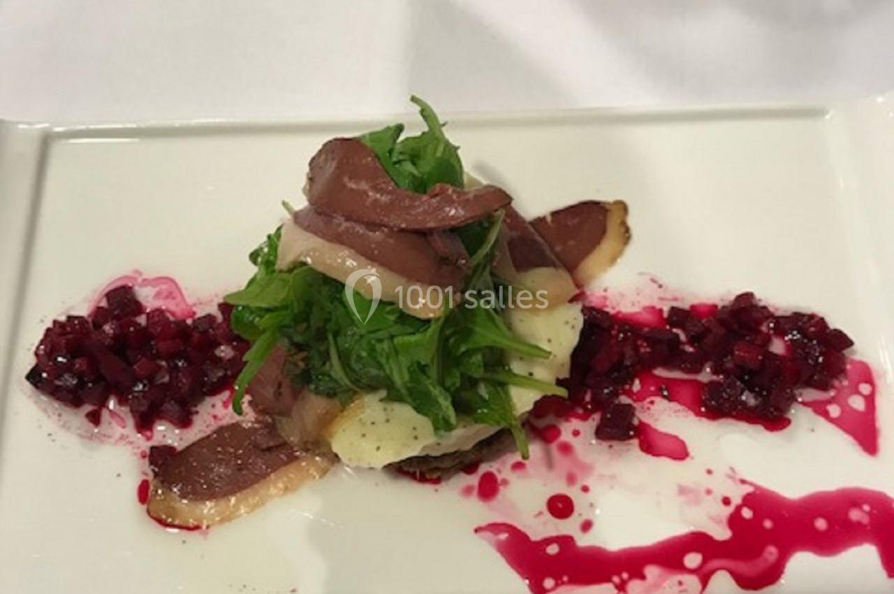 Assiette gastronomique avec salade, tranches de viande, betterave en dés et sauce colorée sur une table dressée.