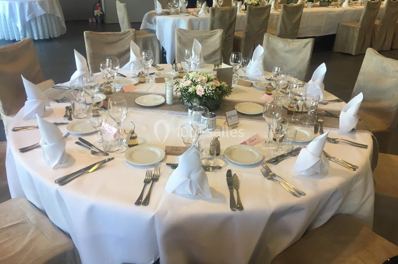 Table ronde élégamment dressée avec nappes blanches, serviettes pliées, vaisselle et centre de table floral.