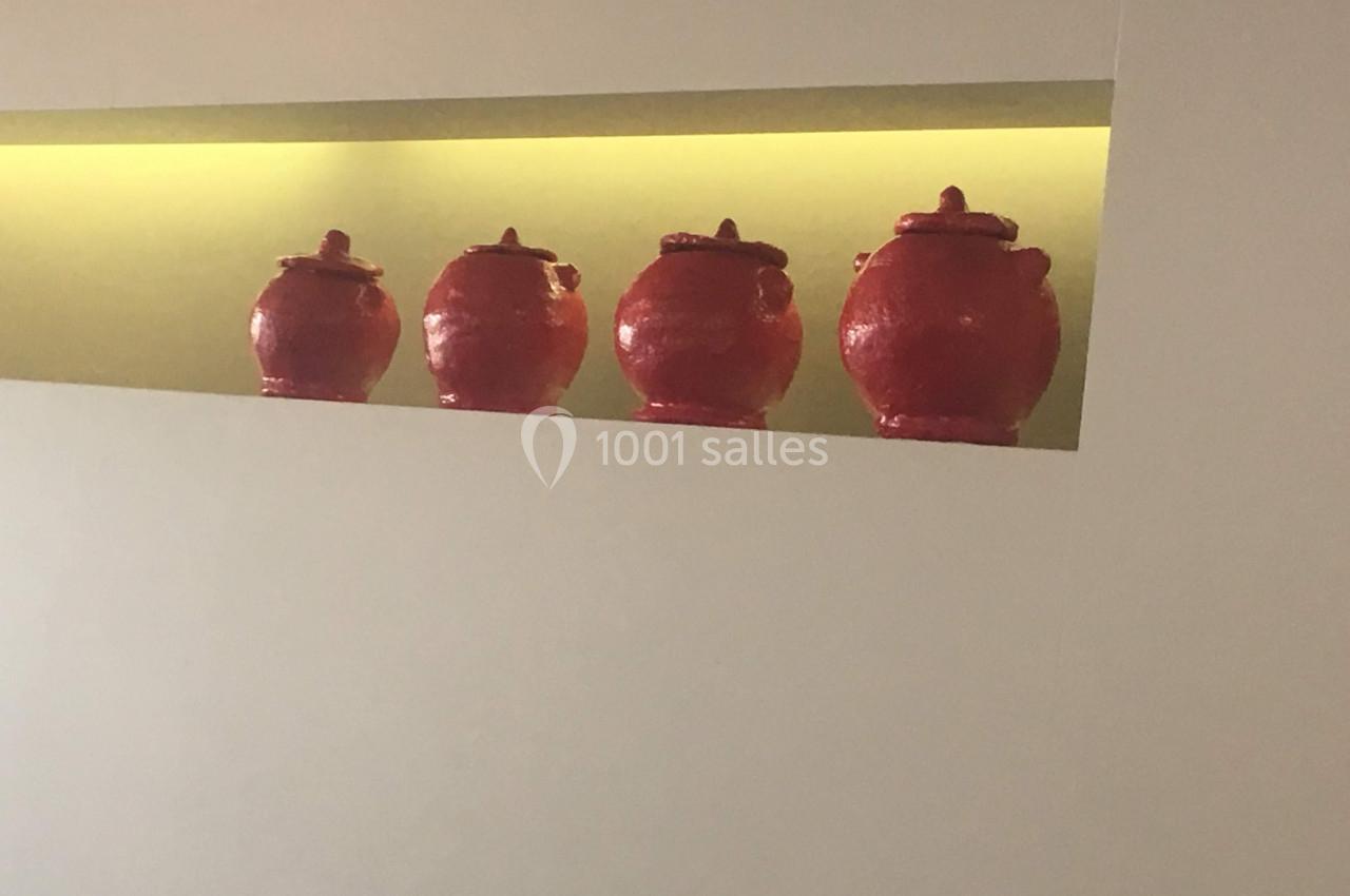 Quatre pots rouges alignés sur une étagère encastrée, éclairée par une lumière jaune douce.
