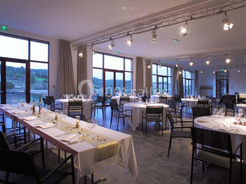 Salle de réception lumineuse avec tables dressées, grandes baies vitrées et vue sur un paysage extérieur.