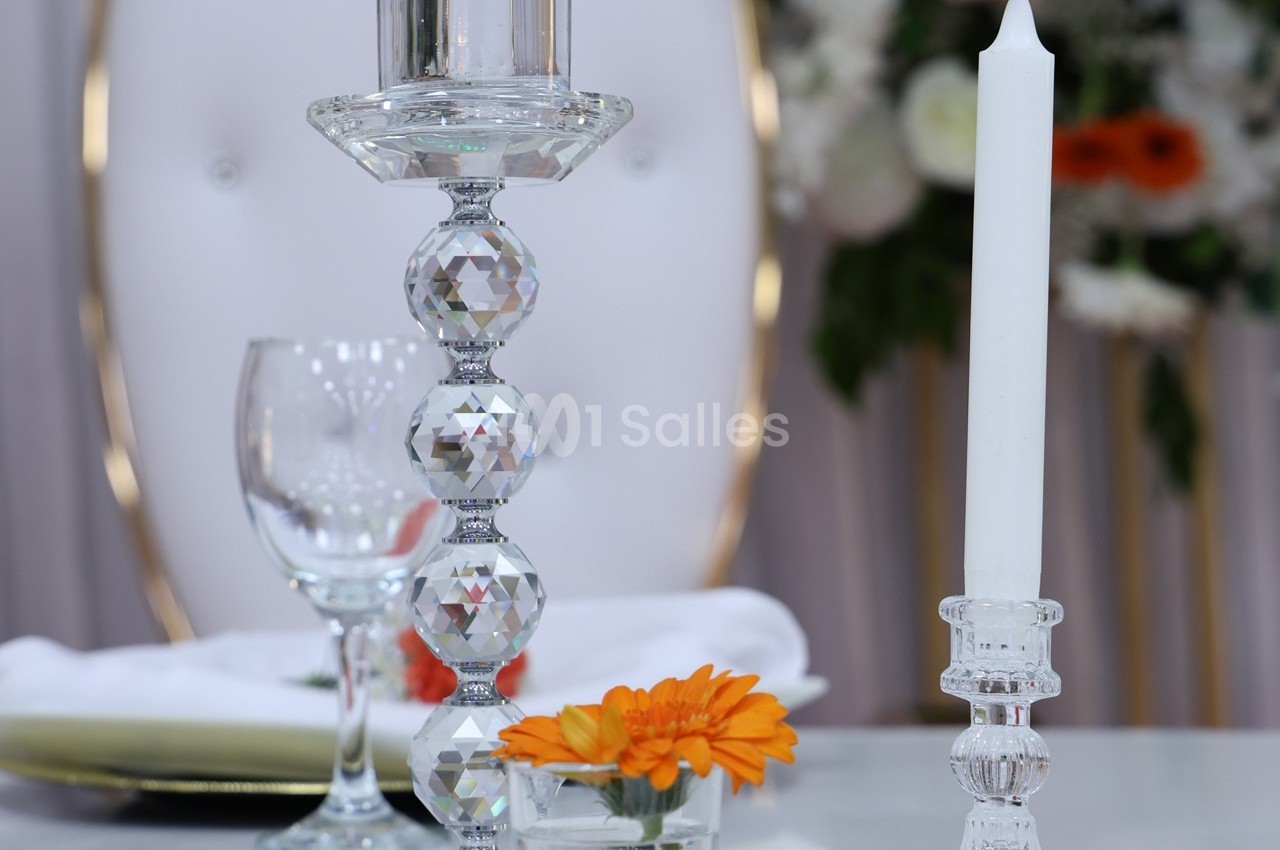 Bougeoirs en cristal avec bougies, verre à pied et fleur orange sur une table décorée, arrière-plan flou.