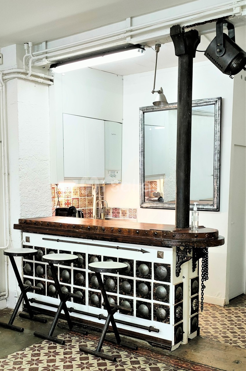 Comptoir de bar vintage avec tabourets pliants, décoré de carreaux anciens, situé dans un espace lumineux.