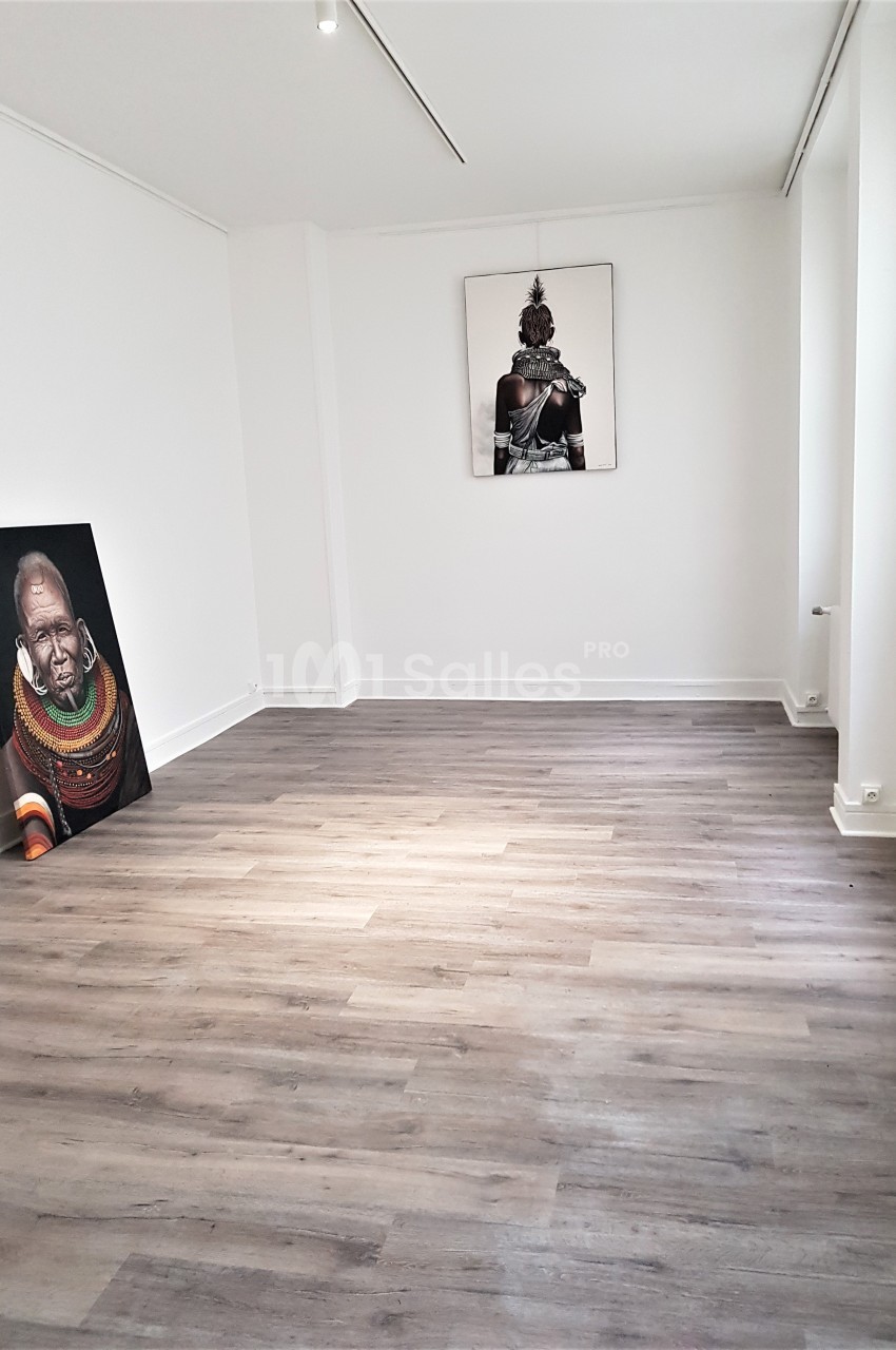 Salle vide avec parquet clair, murs blancs et deux tableaux d'art contemporain posés et accrochés.
