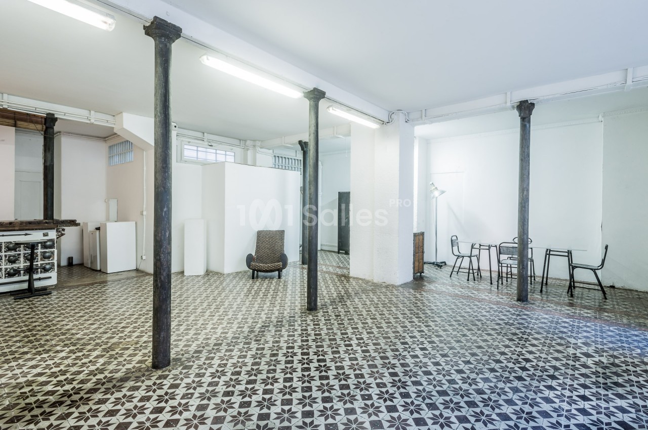 Espace intérieur lumineux avec sol en carreaux de ciment, colonnes métalliques et mobilier minimaliste.