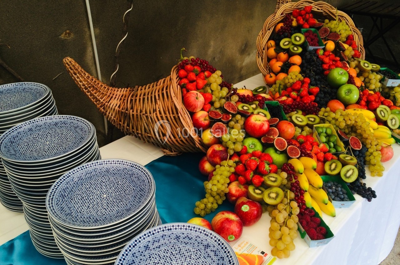 Cornes d'abondance remplies de fruits variés colorés disposés sur une table à côté d'une pile d'assiettes.