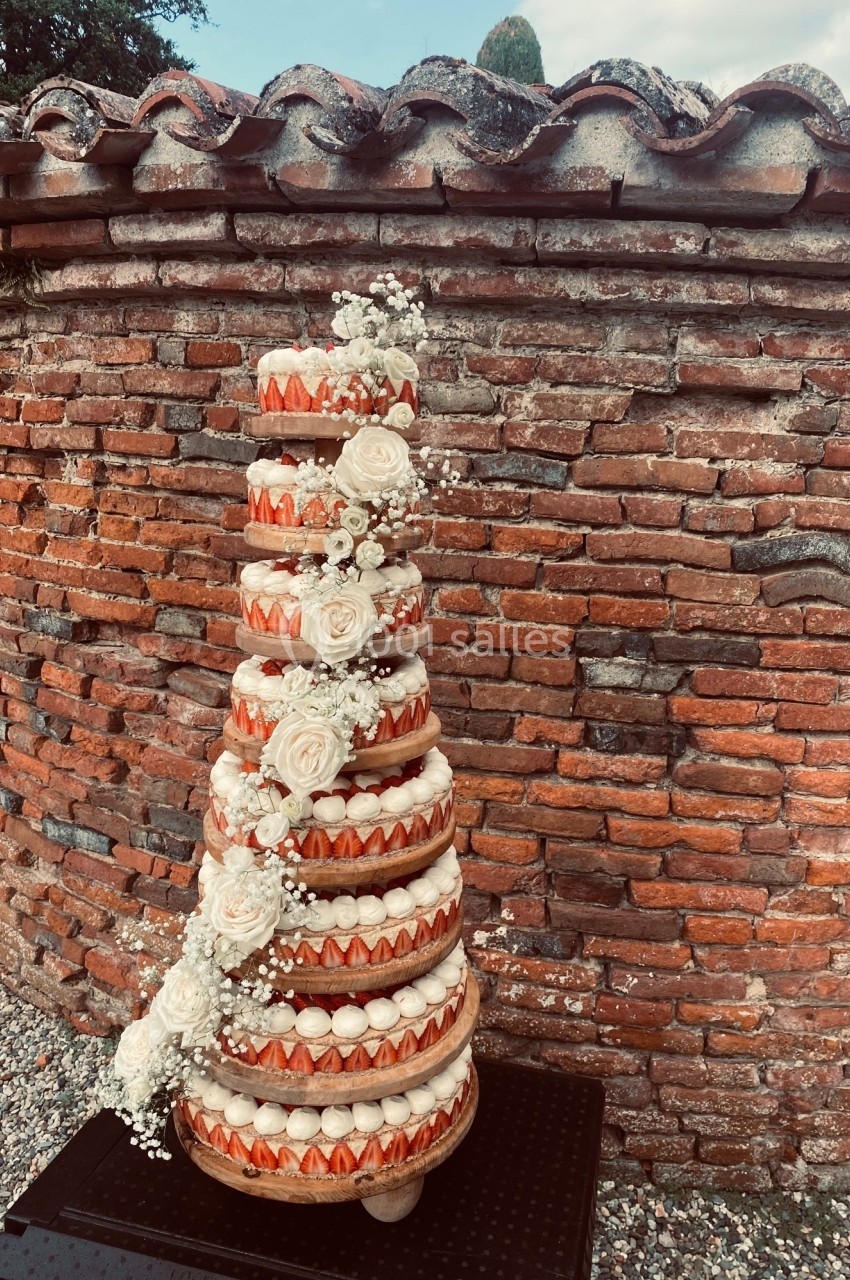 Tour de macarons décorée de fleurs blanches, posée devant un mur de briques rouges en extérieur.
