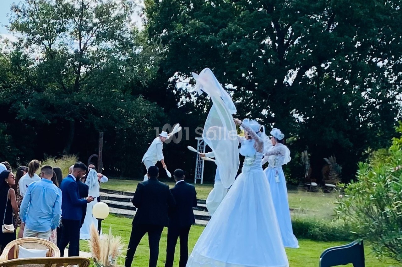 Des artistes sur échasses en costumes blancs performants dans un jardin devant un groupe de spectateurs.
