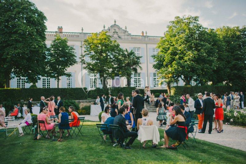 Location salle Piolenc (Vaucluse) - Château Beauchêne #2 Personnes réunies dans un jardin devant un bâtiment élégant, discutant et profitant d'une réception en plein air.