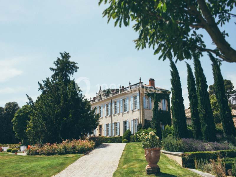 Location salle Piolenc (Vaucluse) - Château Beauchêne #3 Allée gravillonnée menant à une grande maison entourée de jardins paysagers avec arbres et arbustes.