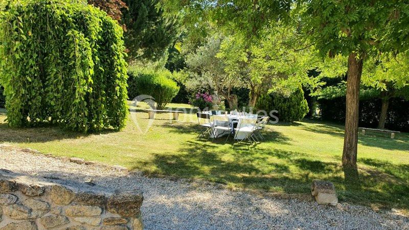Table dressée avec des chaises dans un jardin verdoyant, entouré d'arbres et de buissons sous une lumière ensoleillée.