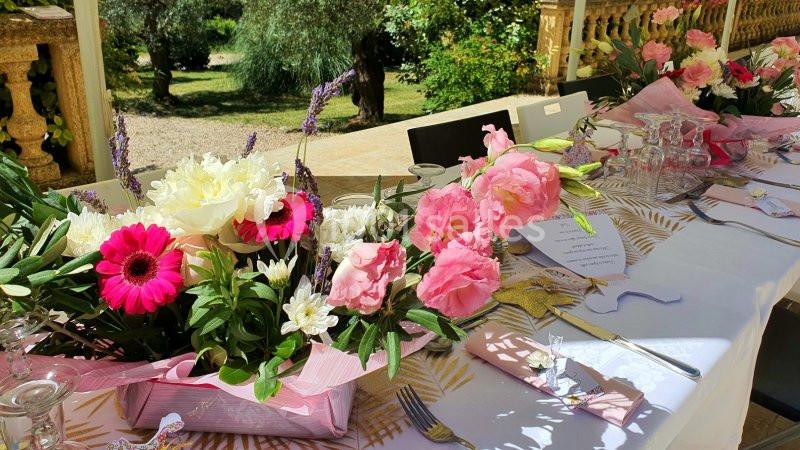 Table décorée avec des fleurs colorées et des accessoires, installée en extérieur avec un jardin en arrière-plan.