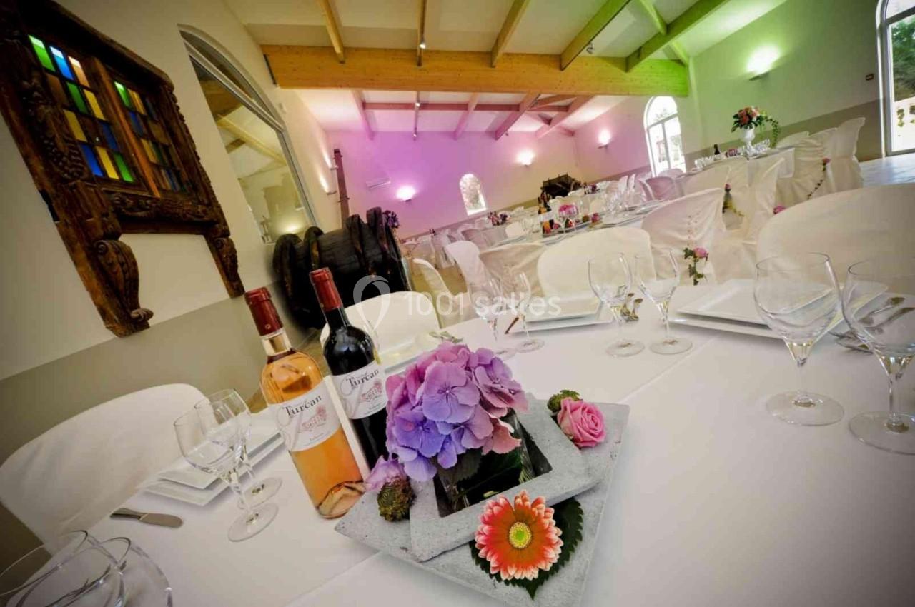 Salle de réception décorée avec des tables dressées, des fleurs en centre de table et des bouteilles de vin.