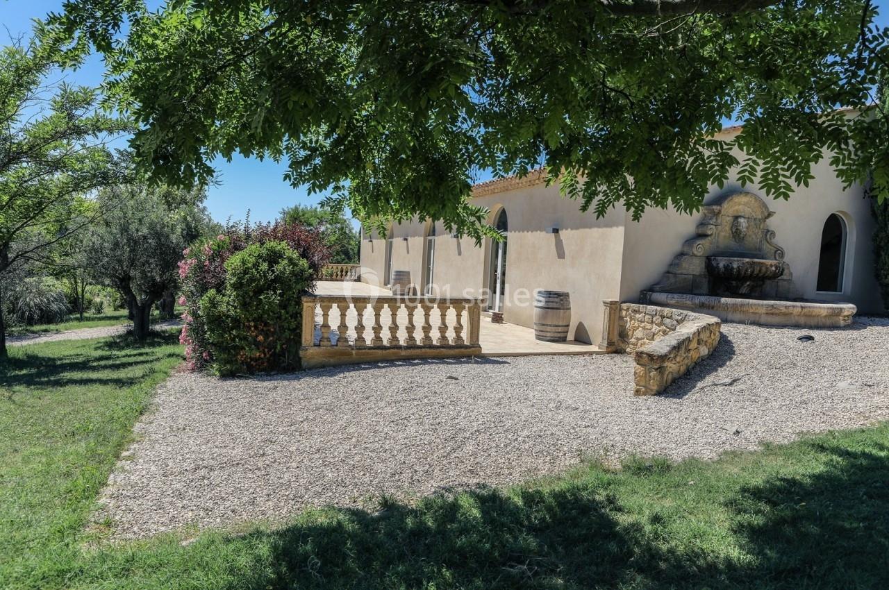 Cour extérieure d'une maison en pierre avec terrasse, balustrade, fontaine et végétation environnante.